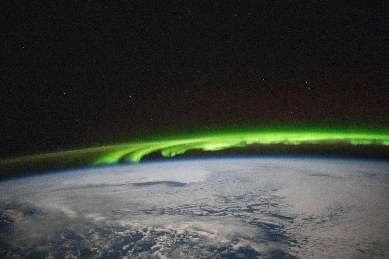 A bright green aurora borealis streams above Earth's surface