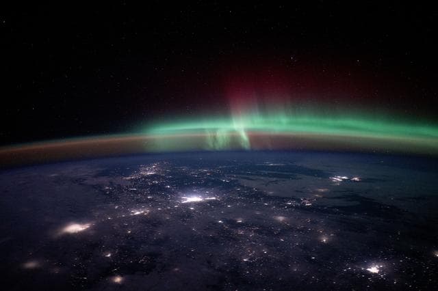 City lights dot the Canadian landscape underneath an aurora