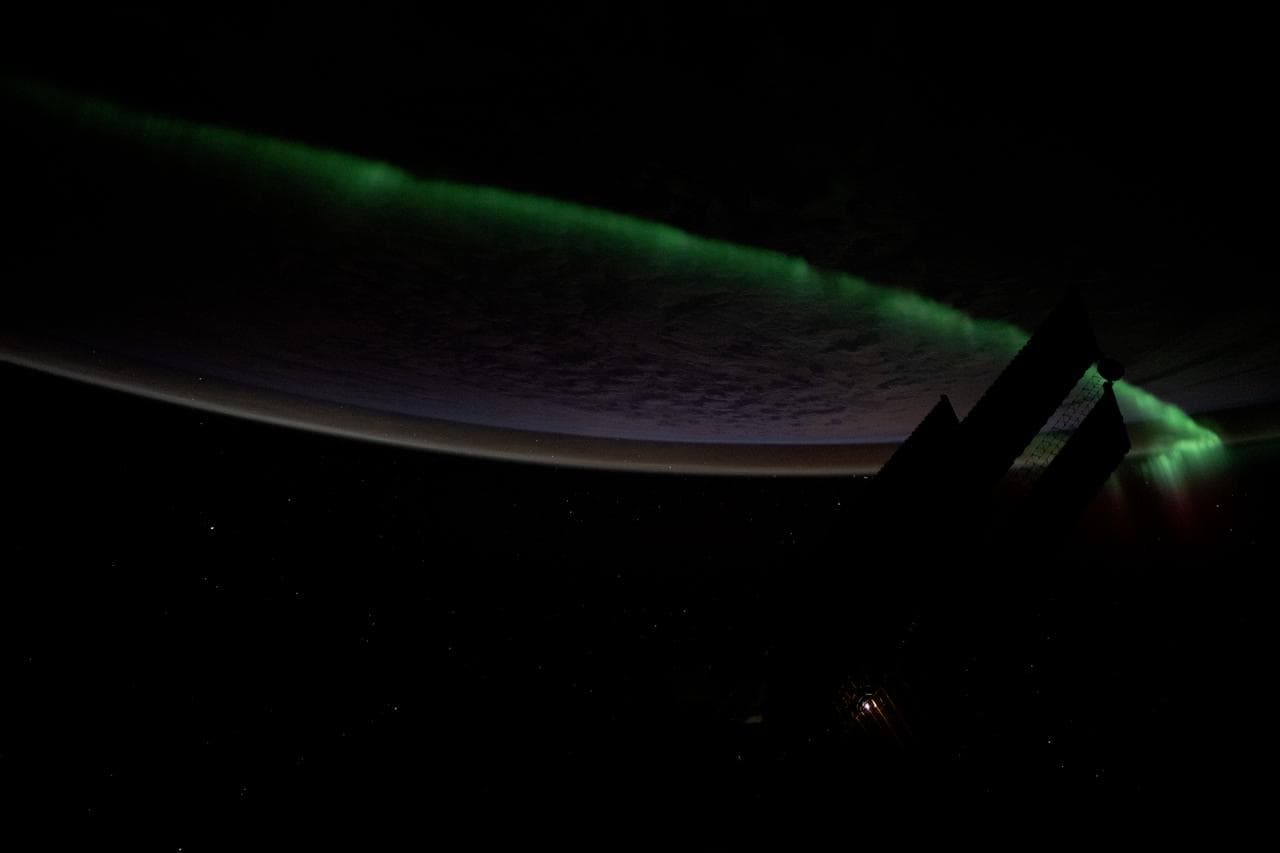 An atmospheric glow crowns Earth's horizon as an aurora streams