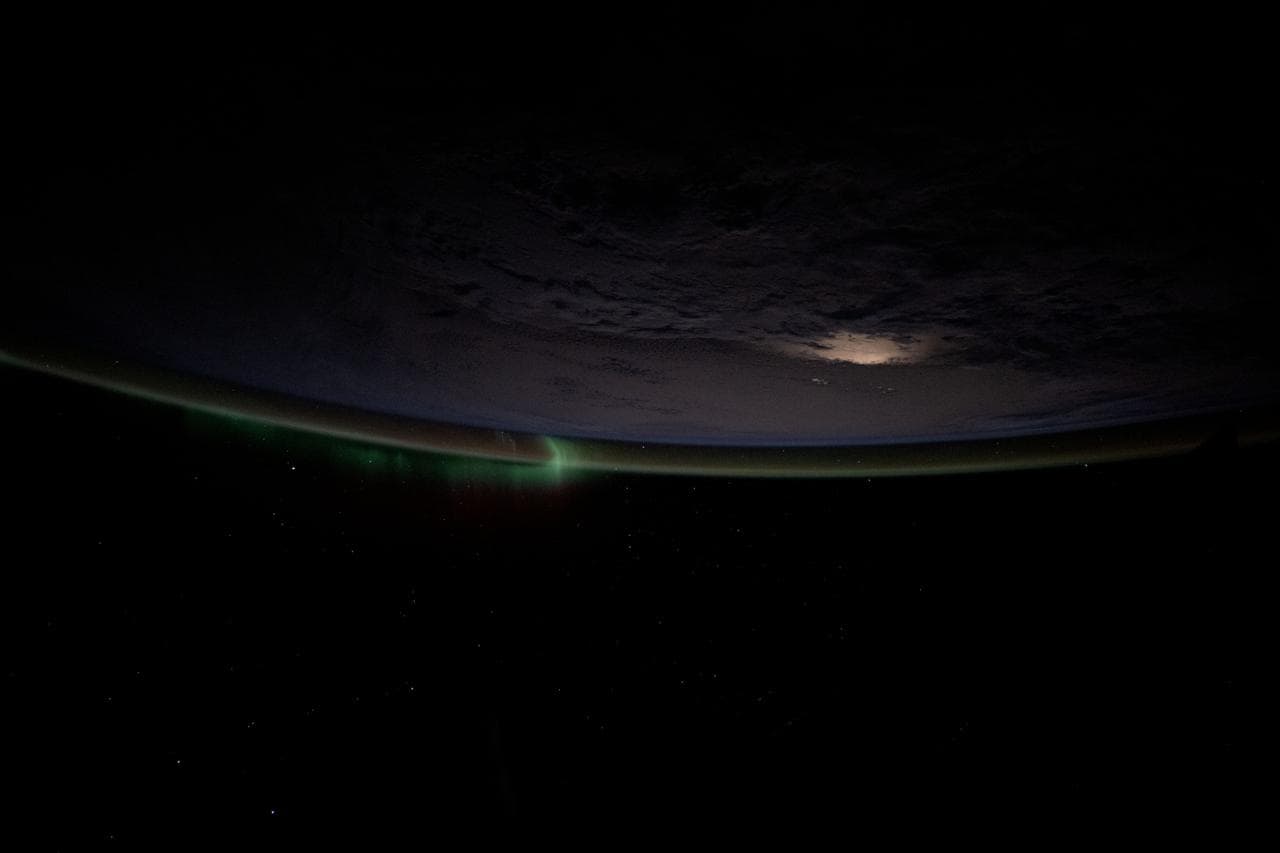 A wispy aurora intersects with Earth's atmospheric glow