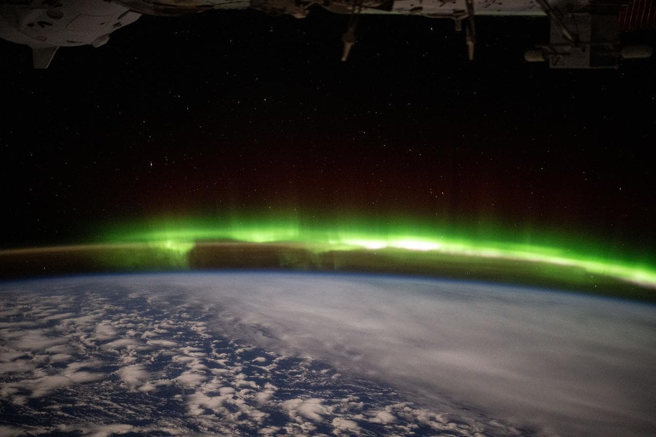 A bright green aurora australis streams above Earth's horizon