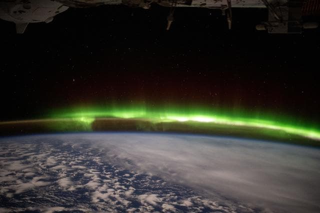 A bright green aurora australis streams above Earth's horizon