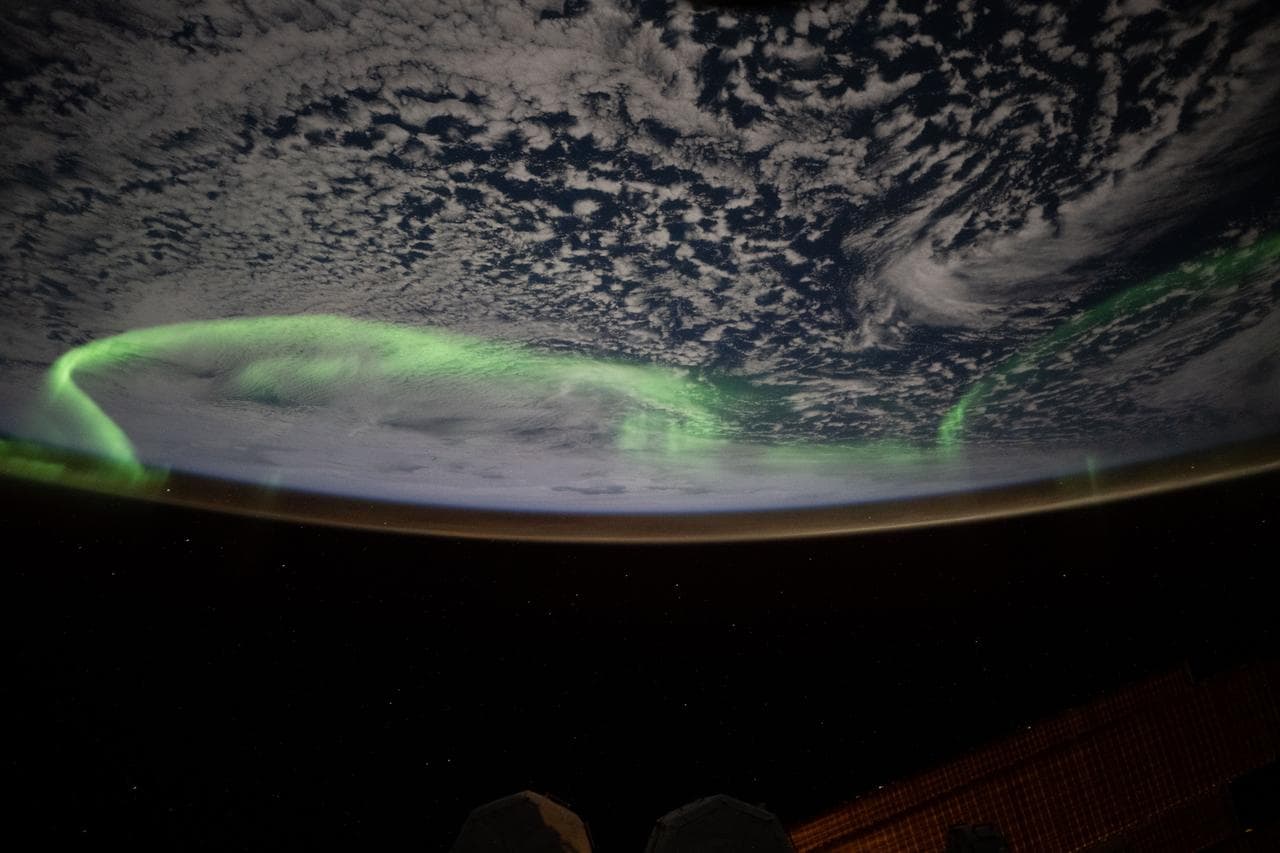 The aurora australis arcs above a partly cloudy Indian Ocean
