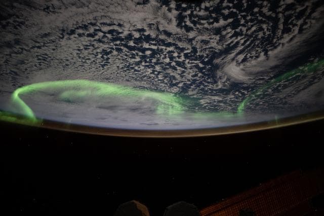 The aurora australis arcs above a partly cloudy Indian Ocean