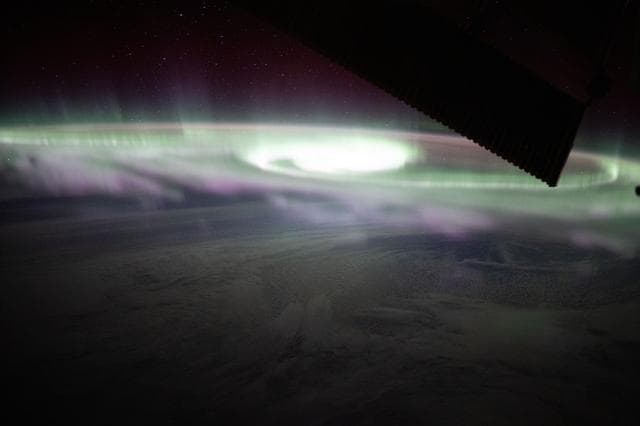 The aurora australis swirls over a cloudy Pacific Ocean
