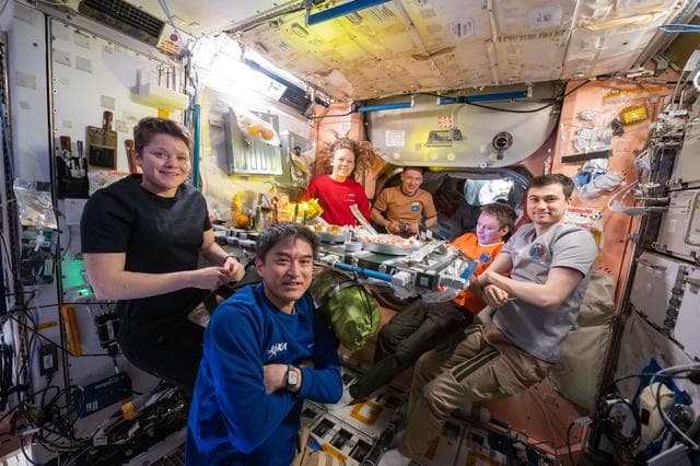 Expedition 73 crew members pose for a portrait during dinnertime