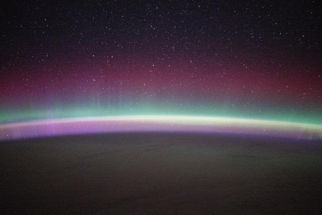 A green and red aurora australis shimmers beneath a starry sky