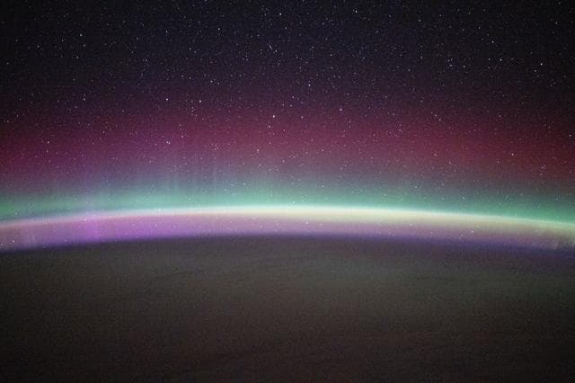 A green and red aurora australis shimmers beneath a starry sky