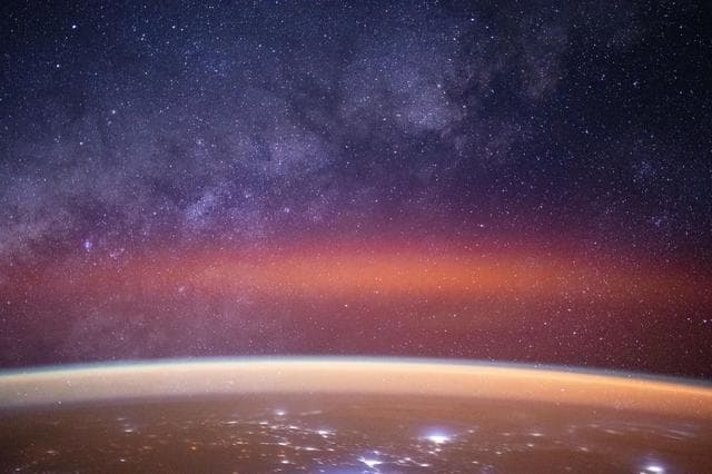 The Milky Way spans the night sky above a bright orange-yellow airglow