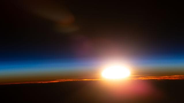 An orbital sunrise illuminates Earth's atmosphere and cloud tops