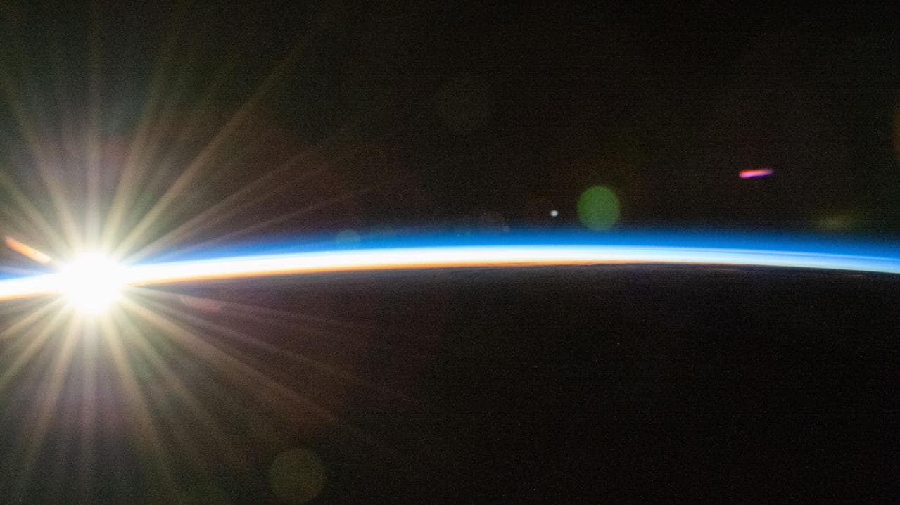 An orbital sunrise bursts above Earth's horizon