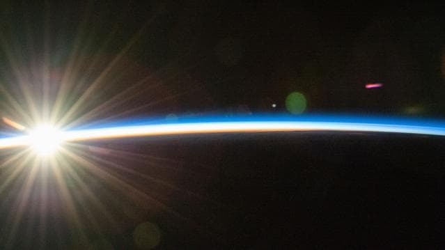 An orbital sunrise bursts above Earth's horizon