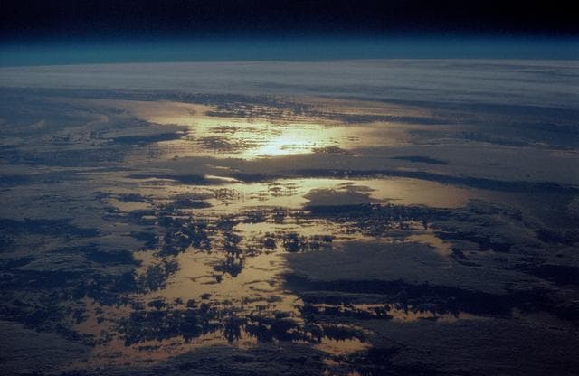 STS-36 Earth observation of sun beaming off cloud-covered ocean waters