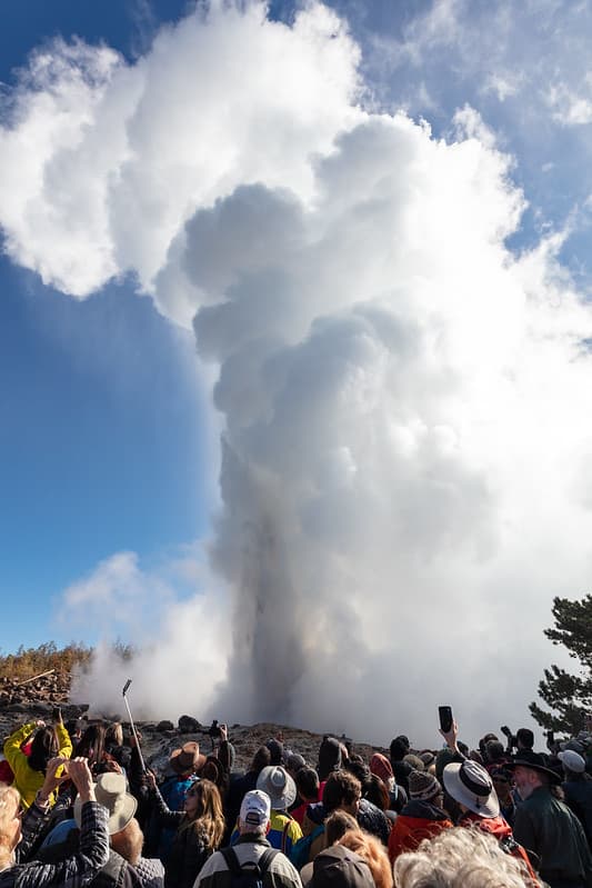 A crowd of people watch and photograph a Steamboat Geyser erupti