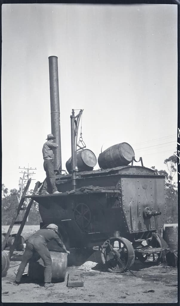 Men loading barrels of tar into tar melting machine