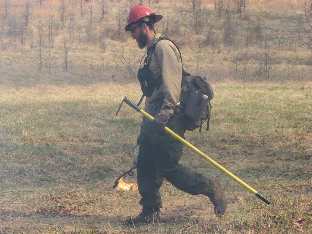 Firefighter with drip torch and hand tool