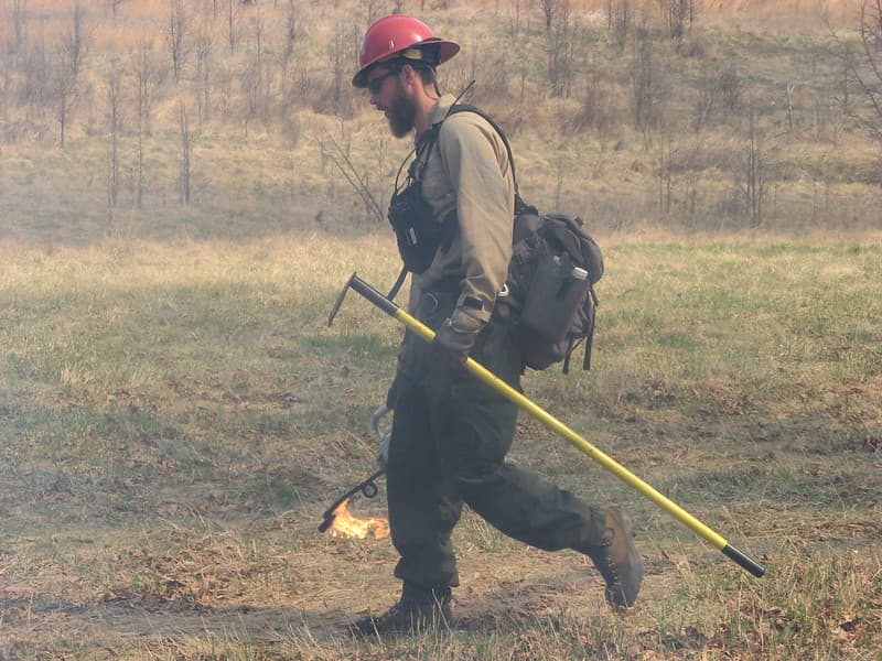 Firefighter with drip torch and hand tool