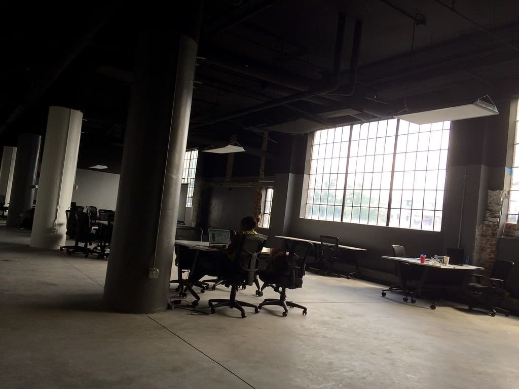 Person Sitting at Office Desk in Warehouse by Pillar