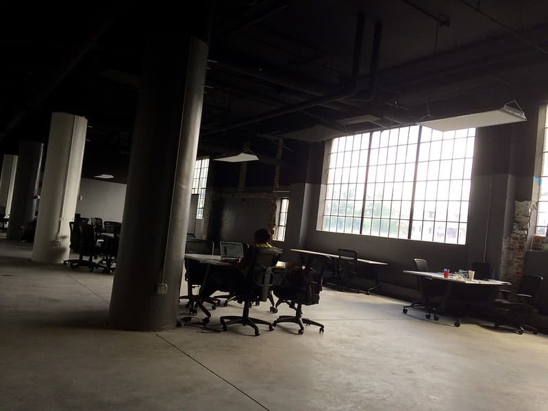 Person Sitting at Office Desk in Warehouse by Pillar