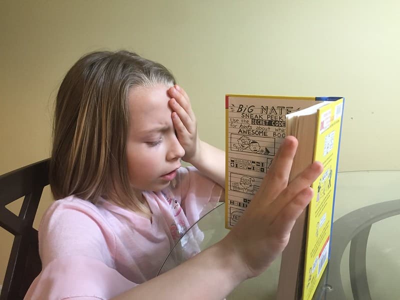Child Reading Book with One Eye Covered
