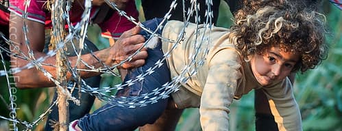 A refugee girl moves under barbed wire