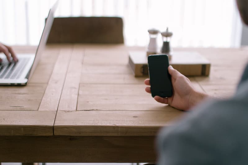 Hand Holding iPhone on Wooden Table