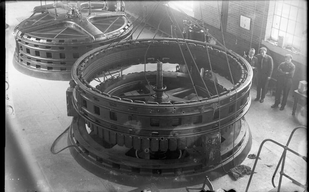 Men beside turbine inside hydro-electric generation plant