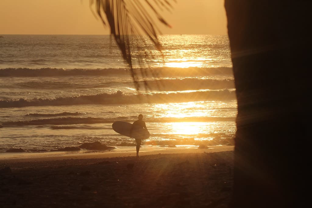 Surfer with Surfboard on Ocean Beach at Sunset