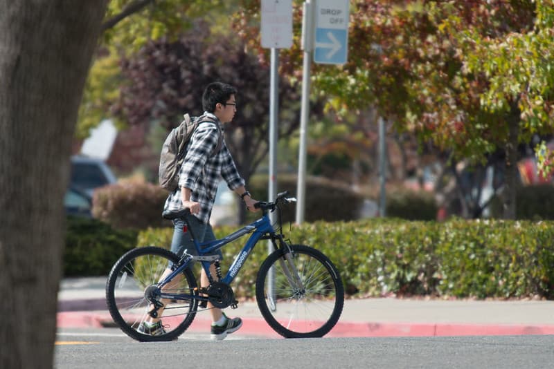 Student walking across road with bicycle